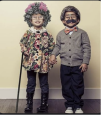 Two kids dressed as a little old lady and a little old man, with gray wigs, glasses, a cane and a drawn-on mustache