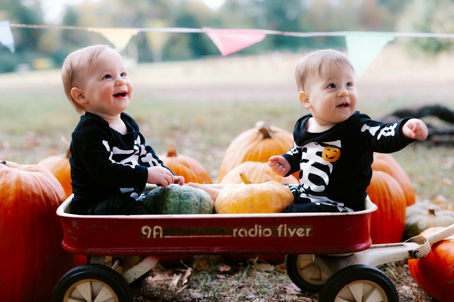 Two babies in skeleton costumes sitting in a wagon with pumpkins
