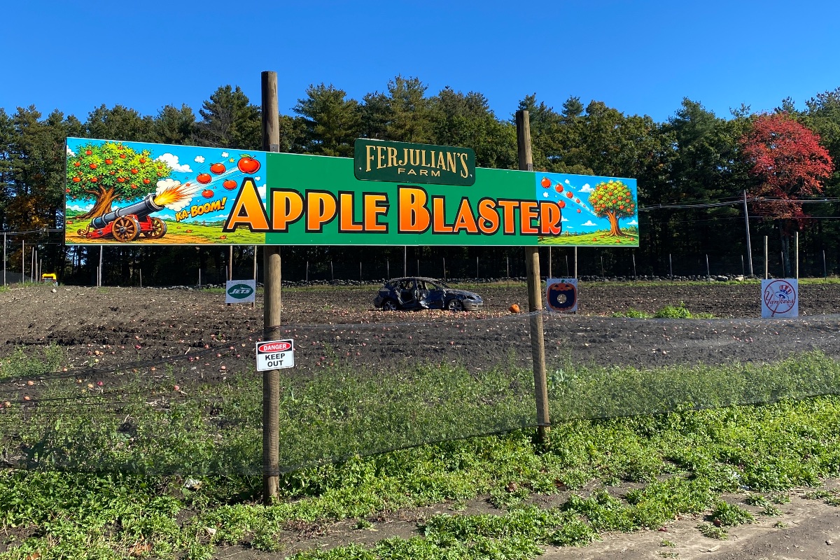 The Apple Blaster sign at Ferjulian’s Farm in Hudson, Massachusetts, with a field of apple targets behind it
